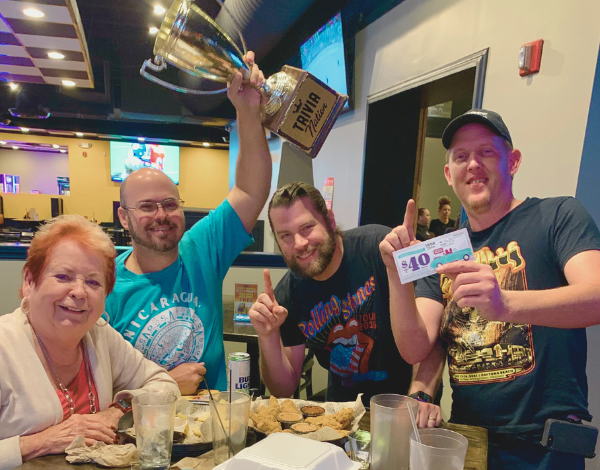 Dick's Wings & Grill Jacksonville FL 32244 trivia night: group of four adults around a table celebrating and smiling with one man holding up a Trivia Nation trophy in the air