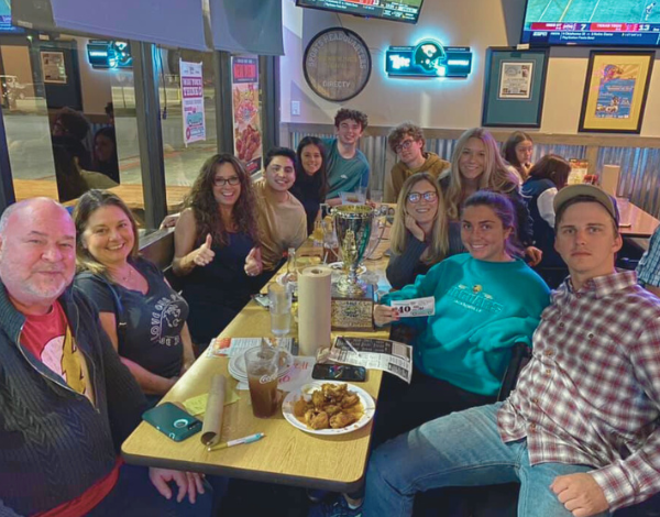 Dick's Wings & Grill Jacksonville FL 32250 trivia night: large group of people including older adults and young seated around a table smiling with a trophy on the table and a plate of wings