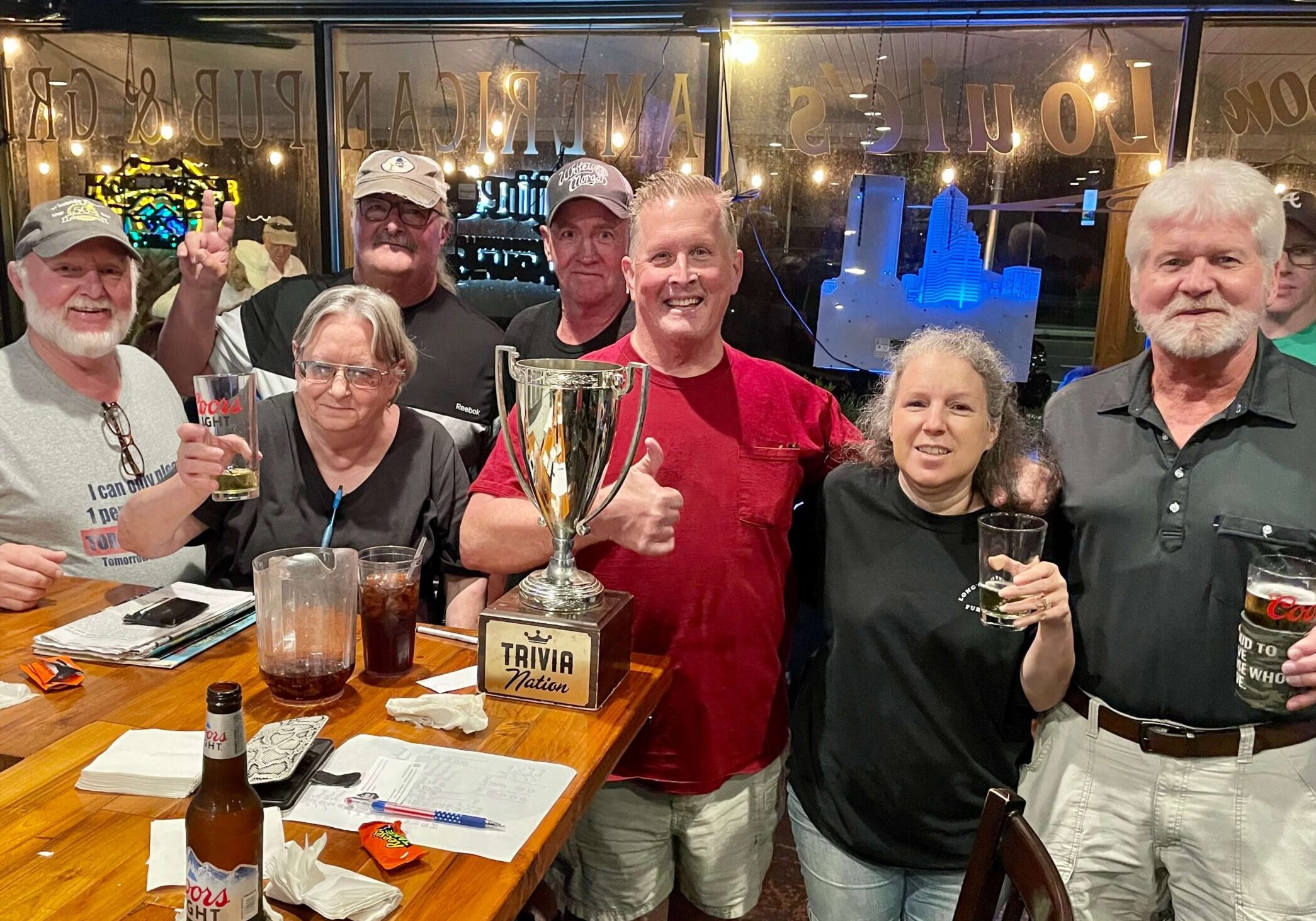 Harps American Pub & Grill Jacksonville FL 32210 trivia night: group of older people at a bar smiling and gathered around a Trivia Nation trophy while raising beer glasses