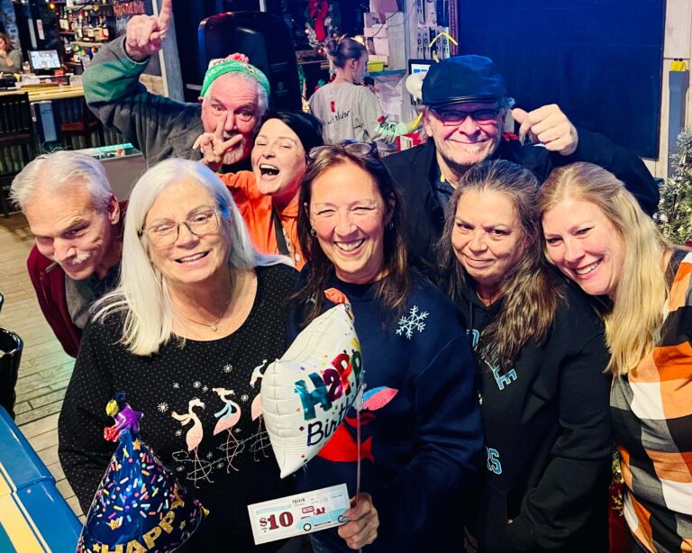 Hurricane Grill & Wings Fleming Island FL 32003 trivia night: group of adults gathered together smiling and celebrating while the woman in front holds up a Happy Birthday balloon and a $10 trivia gift card