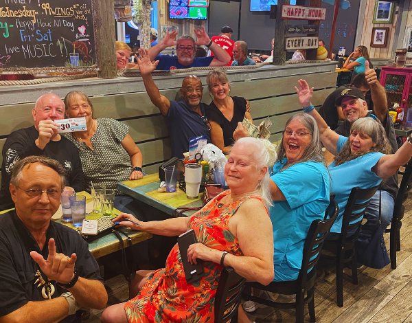 Hurricane Grill & Wings Jacksonville FL 32223 trivia night: group of older people seated together at a long table celebrating with happy expressions and throwing their hands in the air