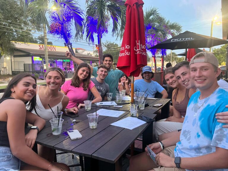 MacDinton's Irish Pub & Restaurant Tampa FL 33606 trivia night: group of young people outside on a patio table smiling with cocktails and a closed umbrella on the table