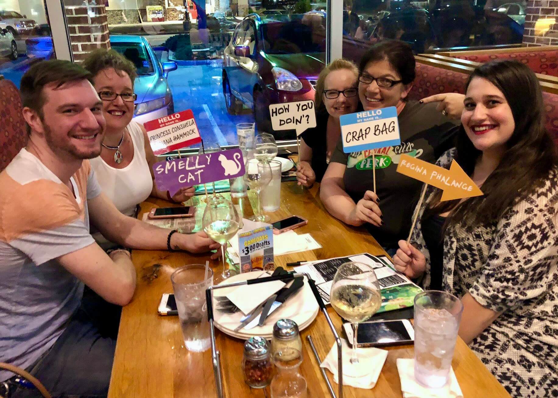 Mellow Mushroom Jacksonville FL 32246 trivia night: group of adults seated around a table having fun and smiling while holding up fun name tag signs for a trivia theme night