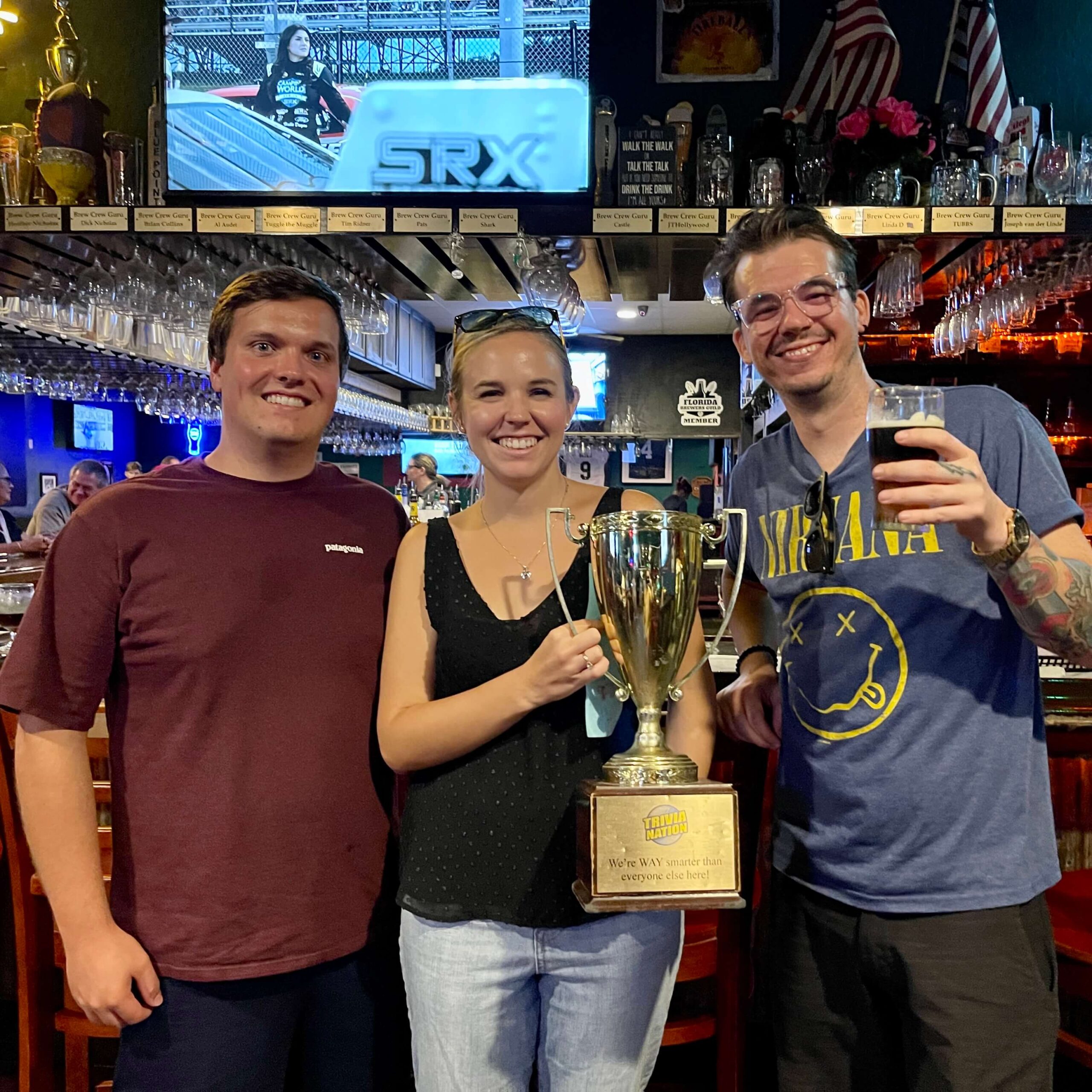 The Broken Barrel Tavern Palm Bay FL 32905 trivia night: two young men and a young woman in between them standing together and smiling while holding up a trophy