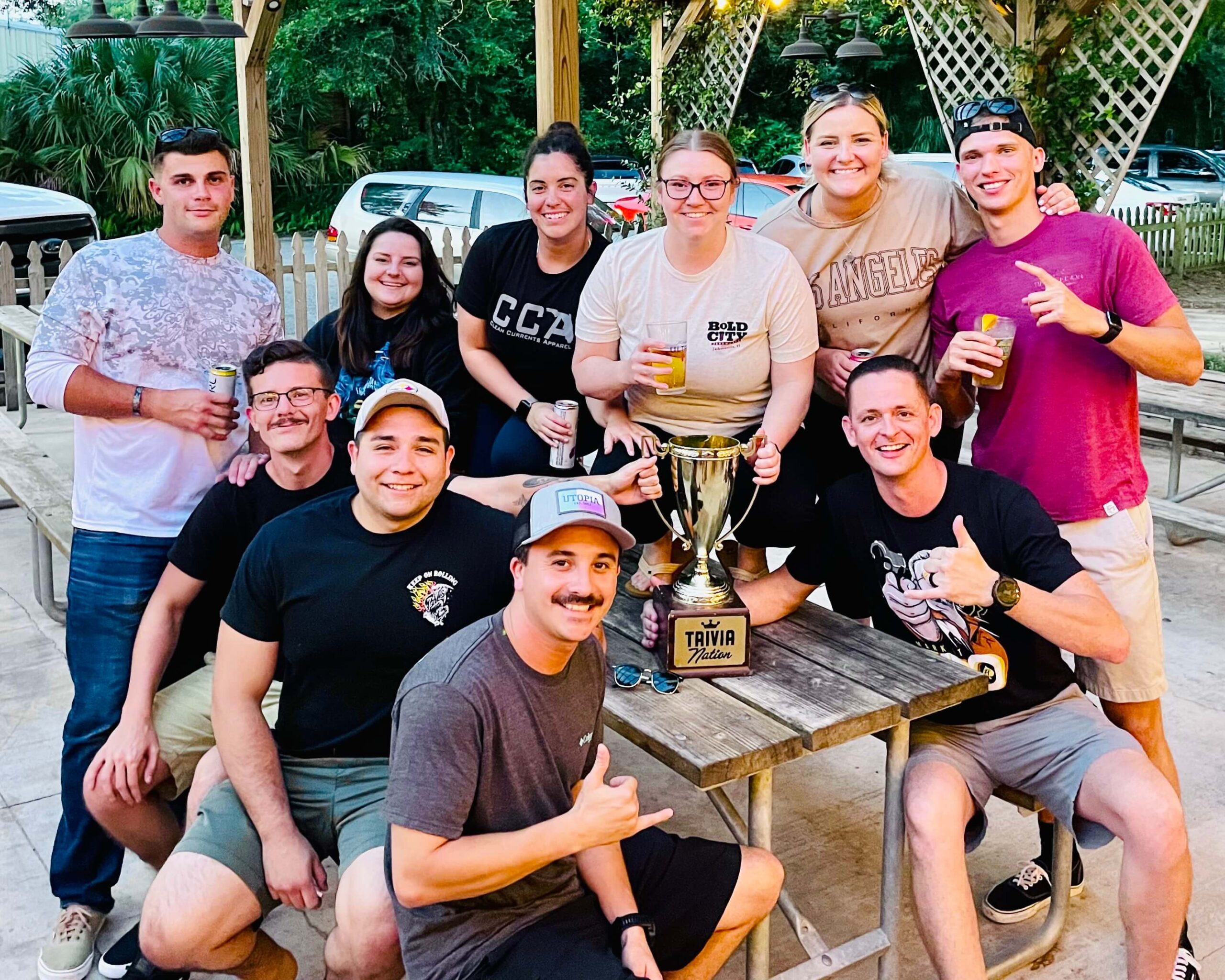 V Pizza & Tap Garden Jacksonville FL 32223 trivia night: large group of young people outside gathered around a patio table smiling with a Trivia Nation trophy in the middle