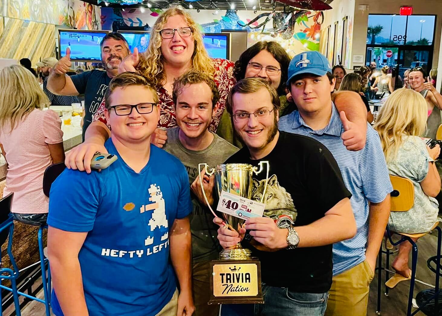 Mellow Mushroom St. Johns FL 32259 trivia night: a group of young adults standing together and smiling while the man in front holds up a Trivia Nation trophy and $40 coupon