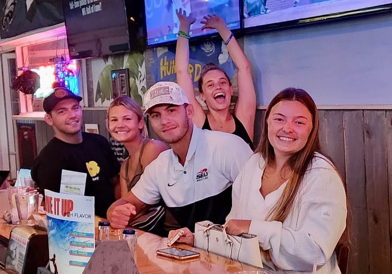 Hurricane Grill & Wings Jensen Beach FL 34957 trivia night: group of young people having fun at the bar with one woman holding her hands up and cheering