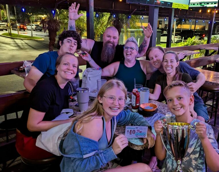Bru's Room Pompano Pompano Beach, FL 33062 trivia night: large group of people outside on a patio with a young boy in the front holding a trophy next to a teenage girl holding a $40 coupon