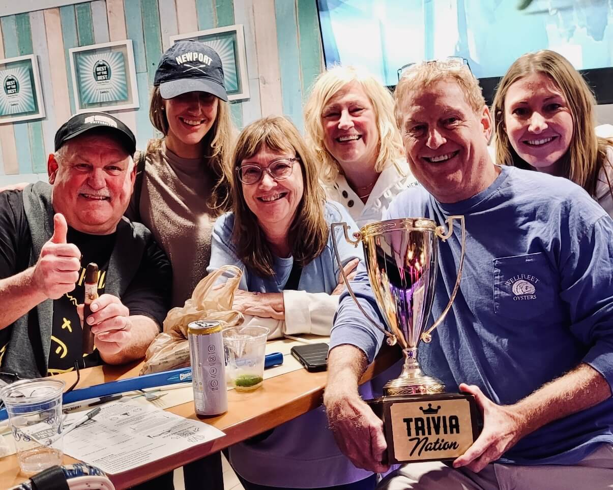 Caddy's Treasure Island FL 33706 trivia night: group adults from young to older gathered around a table together smiling while the man in front holds up a Trivia Nation trophy