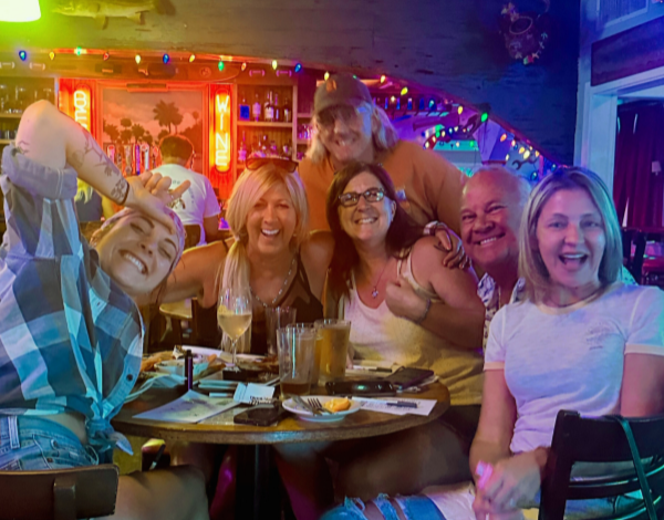 Conchy Joe's Seafood Jensen Beach FL 34957 trivia night: group of people gathered at a table having fun with drinks and wine and a bar with lights behind them