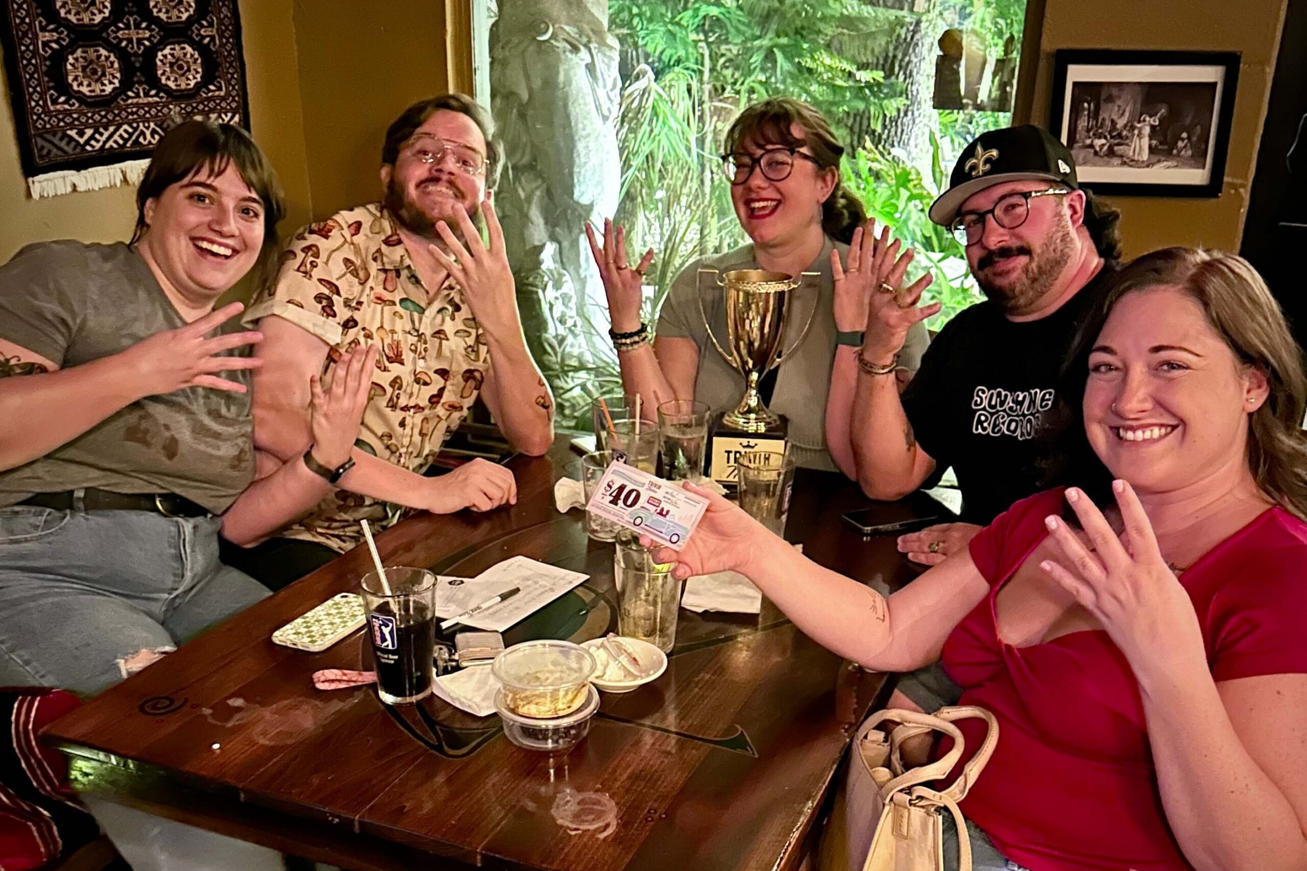 The Casbah Cafe Jacksonville FL 32205 trivia night: group of young adults seated around a table smiling and holding up their hands in celebration with a Trivia Nation trophy and drink glasses on the table