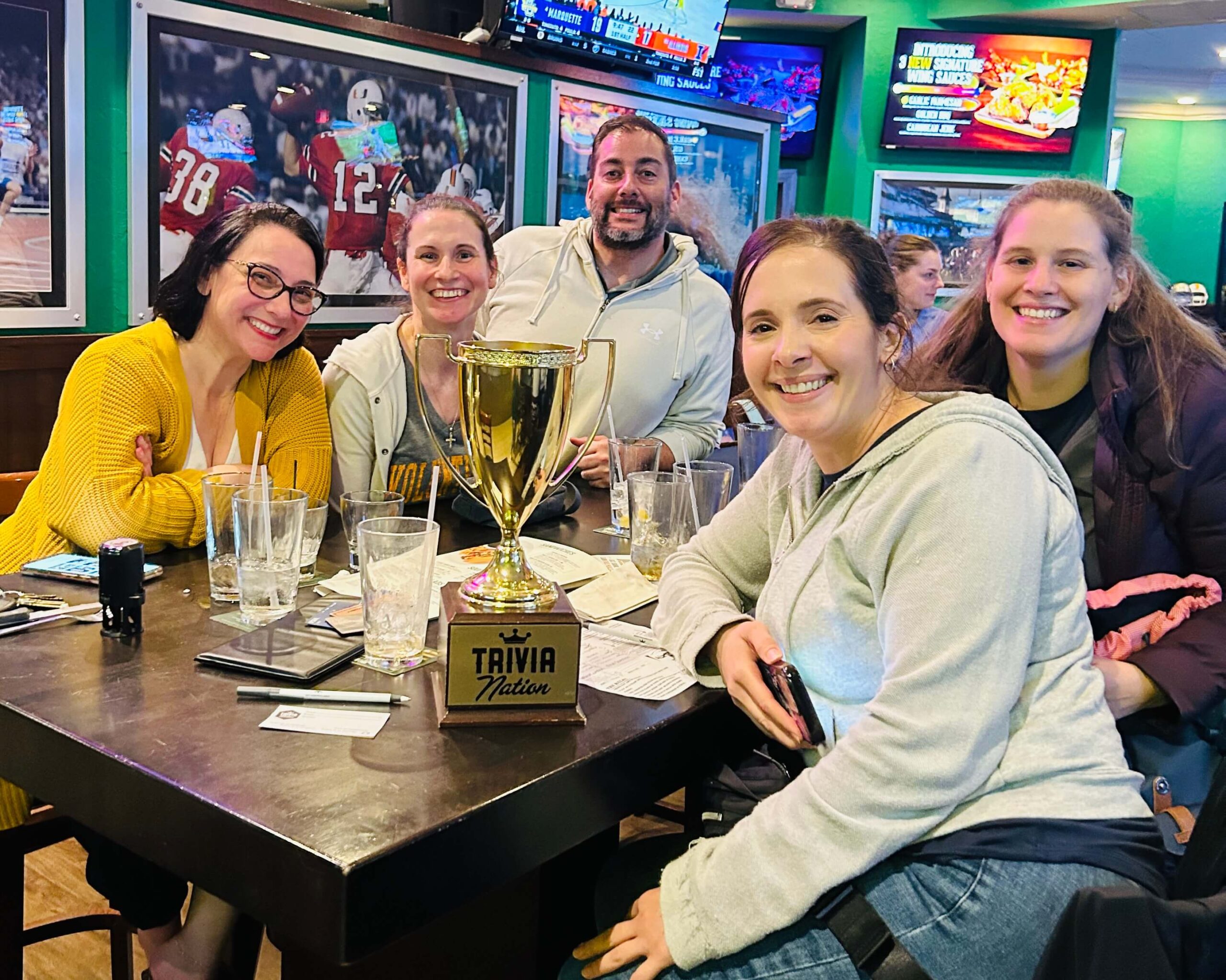 Duffy's Sports Grill Boca Raton FL 33498 trivia night: group of women adults and one man seated together around a table smiling with empty glasses on the table and a Trivia Nation trophy in between them