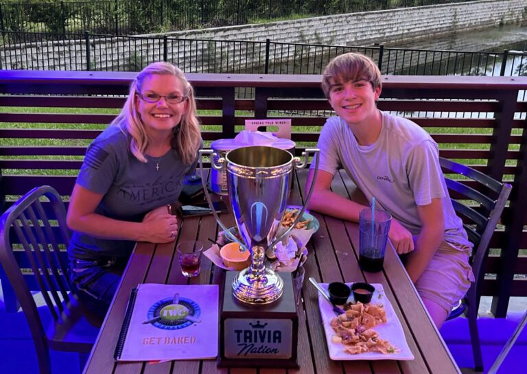 Island Wing Company Jacksonville FL 32259 trivia night: woman and young man smiling at a table outside on a patio with a waterway and a highway behind them