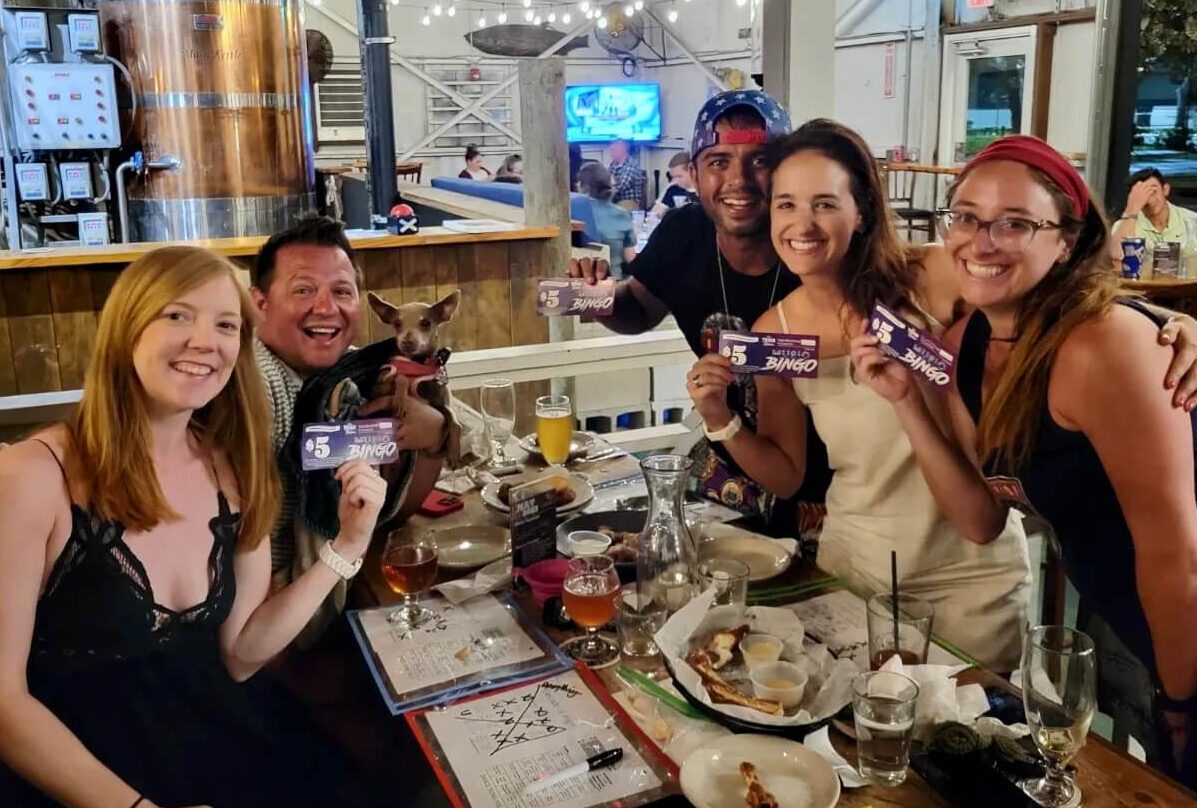 Tarpon River Brewing Fort Lauderdale FL 33301 trivia night: group of young people smiling and holding up bingo coupons with one man holding a small dog