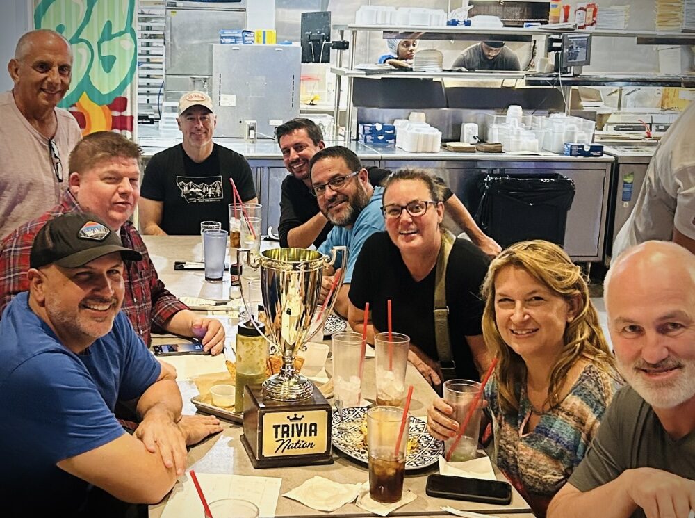 Burrito Gallery Jacksonville FL 32256 trivia night: large group of people seated around a long table smiling with menus and a Trivia Nation trophy on the table