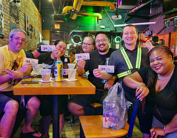 My Tap Room Jacksonville FL 32256 trivia night: group of people gathered around a table and smiling while holding up $30 trivia coupons and having drinks on the table