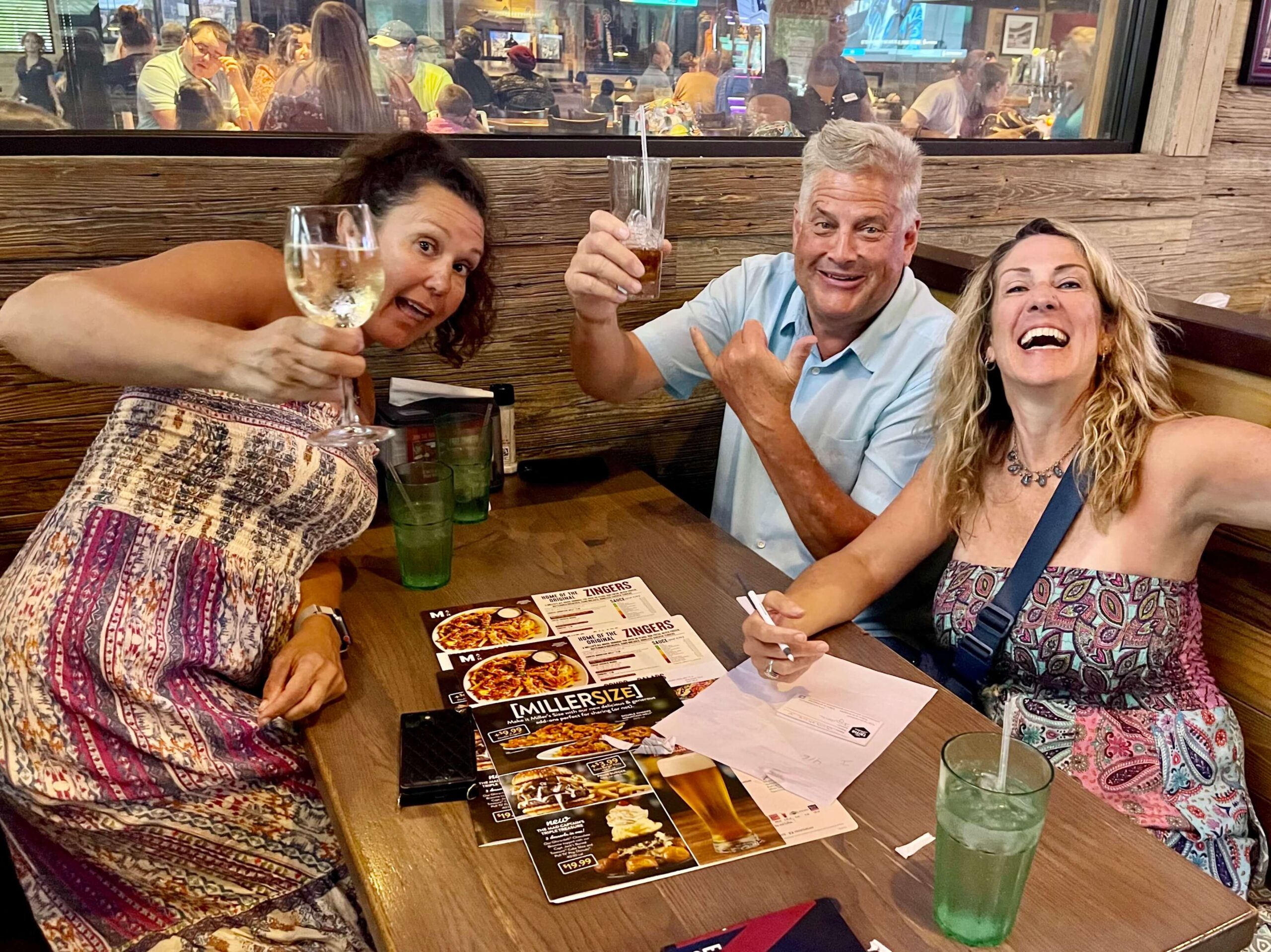 Miller's Ale House Jacksonville FL 32256 trivia night: two women and a man seated at a booth celebrating and having fun while raising their glasses with Miller's Ale House menus on the table between them