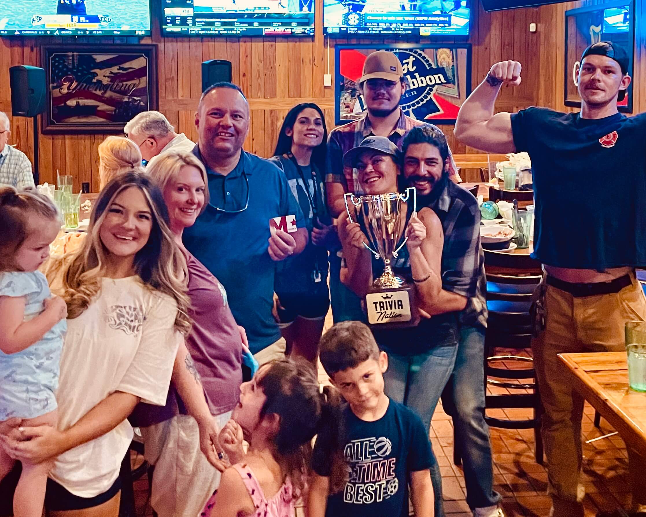 Miller's Ale House Orange Park FL 32073 trivia night: group of adults and family gathered together smiling with kids in the front and a man making a strong arm gesture in the back