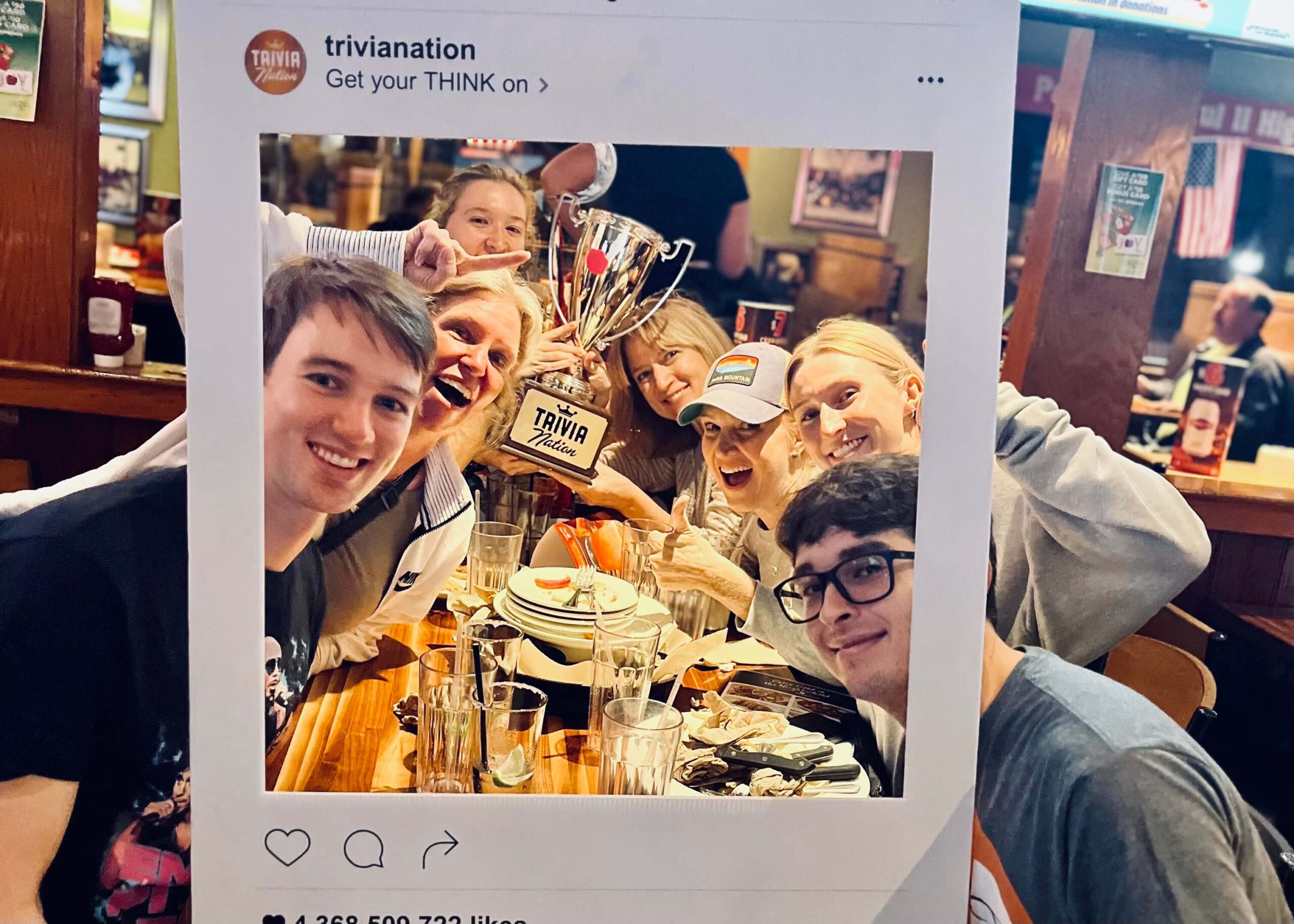 Applebee's Grill & Bar Delray Beach FL 33446 trivia night: group of young adults and women gathered together around a table smiling and making excited expression with a Trivia Nation trophy and Instagram polaroid prop