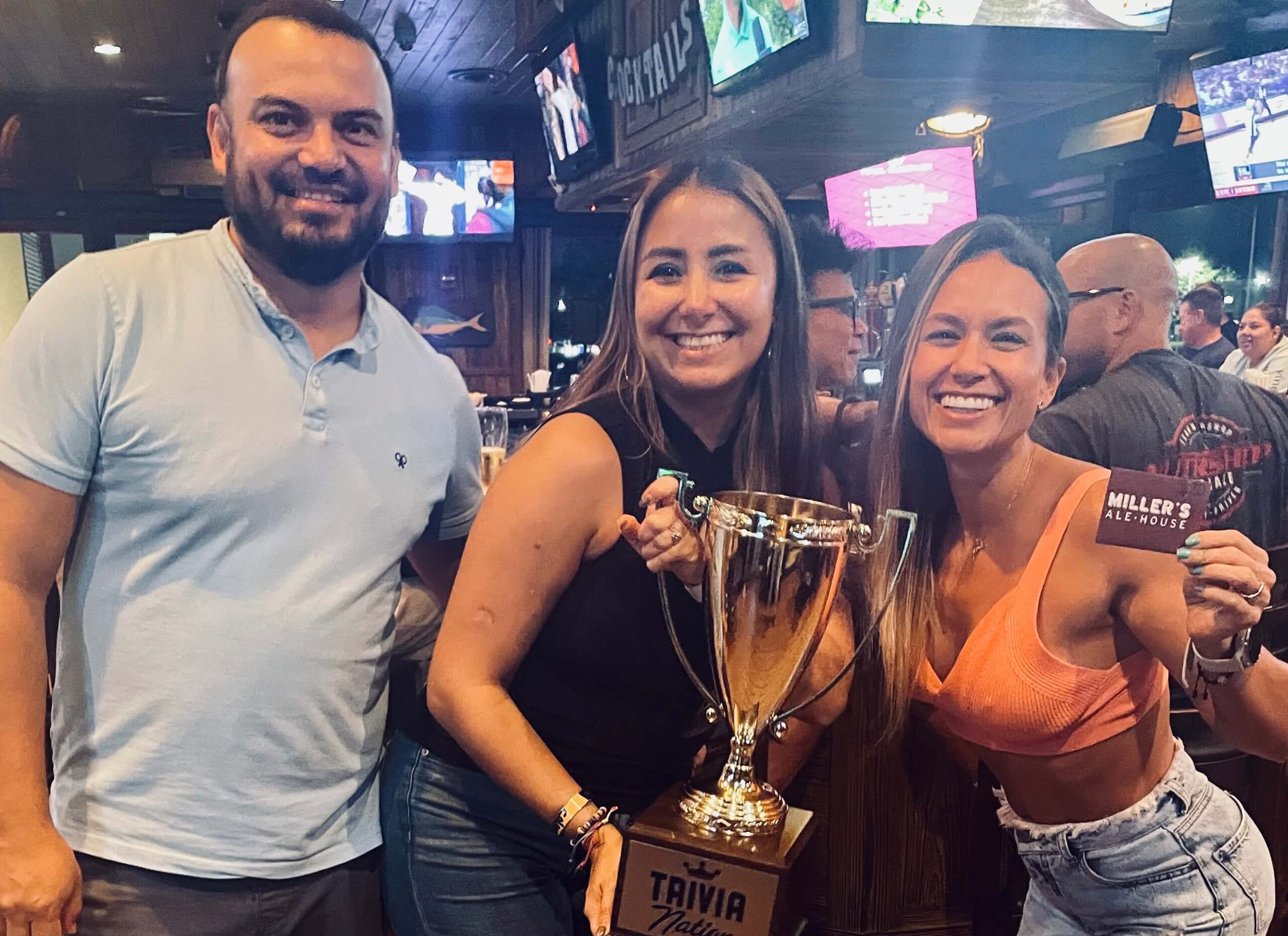 Miller's Ale House Jacksonville FL 32224 trivia night: a man and two women standing together in the restaurant smiling while the women hold up a Trivia Nation trophy and a gift card